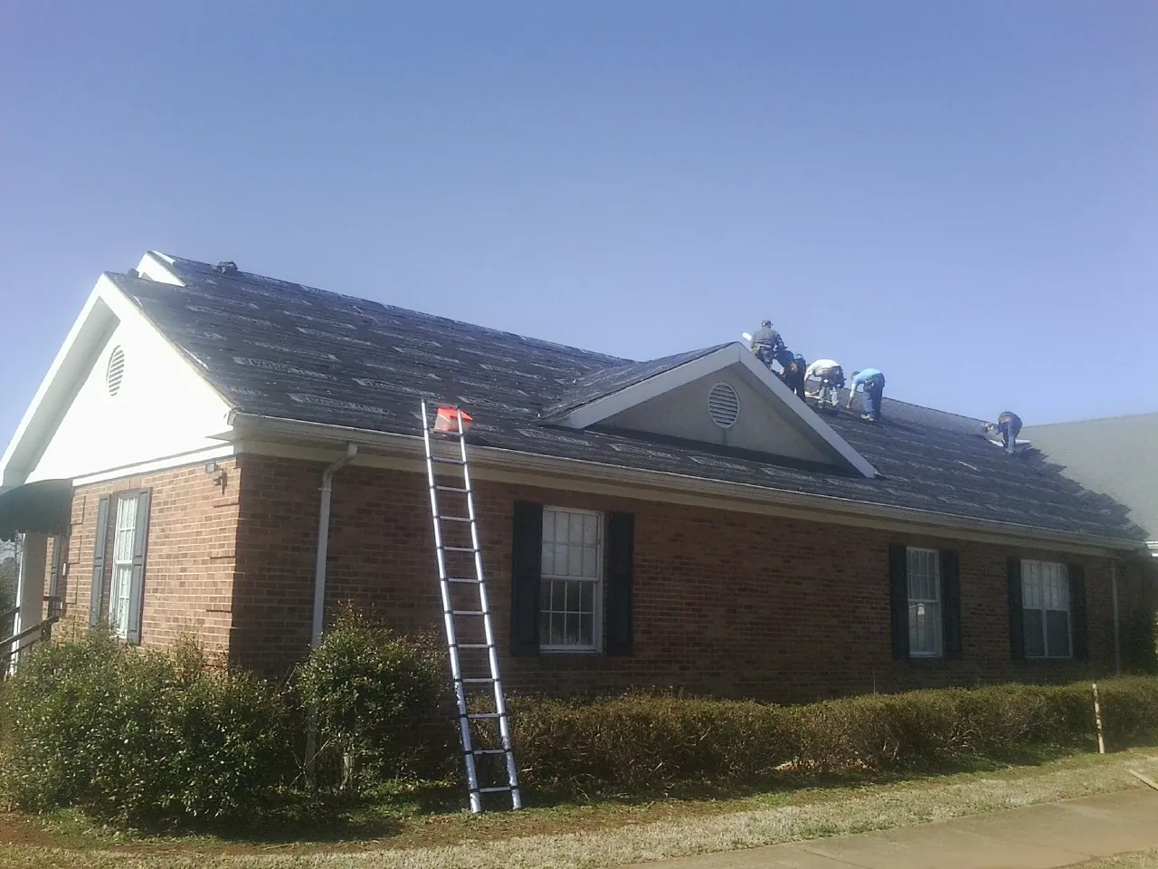 Crew tearing shingles off a brick ranch roof with a ladder set — Metal Roof Repair work by our crew in Media