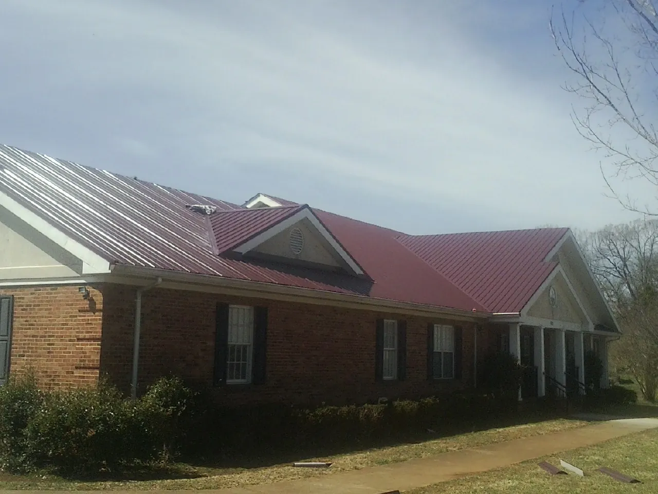 Red metal roof with gabled entries on a long brick building, from a Hail Damage Roof Repair job in Media