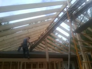 Rafters going up over a new addition with a worker on the wall in Media
