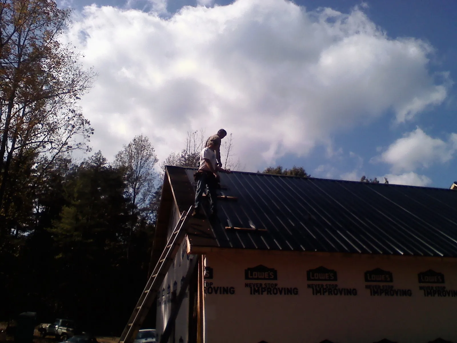 Roofer fastening dark metal panels high against a cloudy sky, from a Roof Inspection job in Media