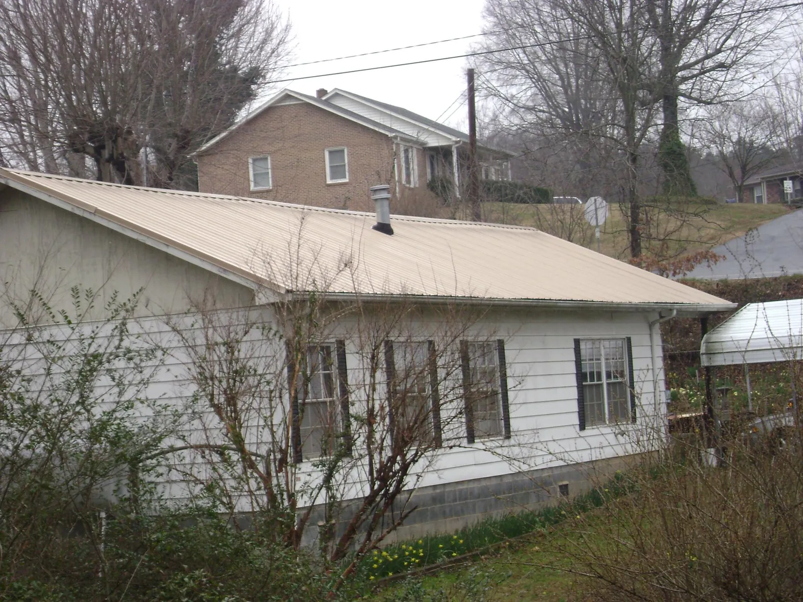 Tan metal roof on a white sided house set into a hillside — Commercial Roofing by Roofing Brothers in Media